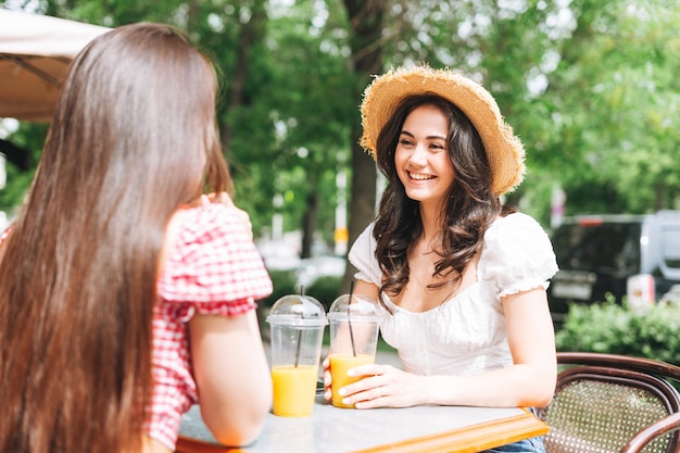 夏のカフェのテラスで話している幸せな笑顔の美しいブルネットの若い女性