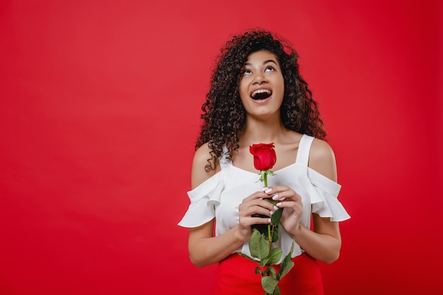 Happy smiling black woman with red rose in hand isolated over red