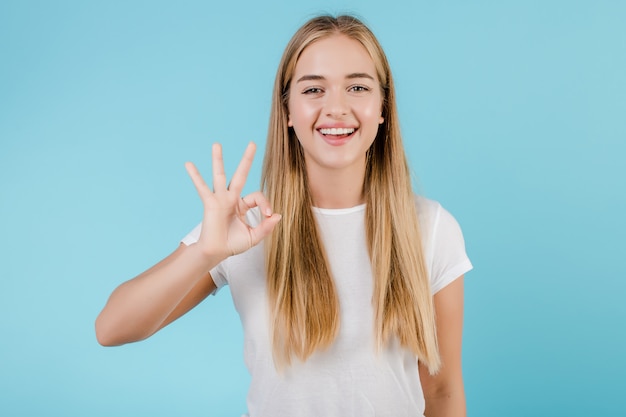 Happy smiling blonde girl showing ok gesture isolated over blue