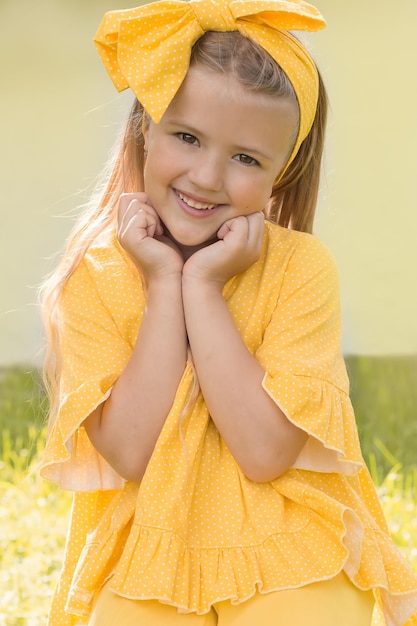 Happy smiling blonde girl with a yellow bow on her head and a dress