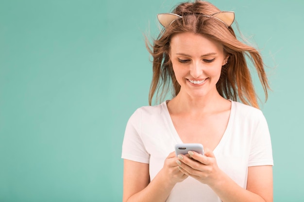 Happy smiling blonde teen girl looking on smartphone on blue background