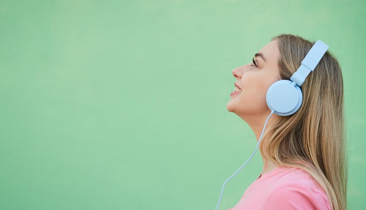 ピンクのシャツを着た幸せな笑顔の金髪の女性は、背景に対して青いヘッドフォンで音楽を聴きます