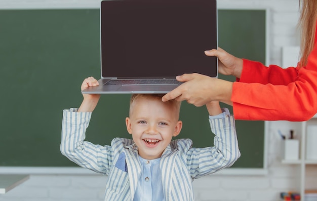 Счастливый улыбающийся мальчик держит ноутбук на голове во время онлайн-урока в классе онлайн-образования