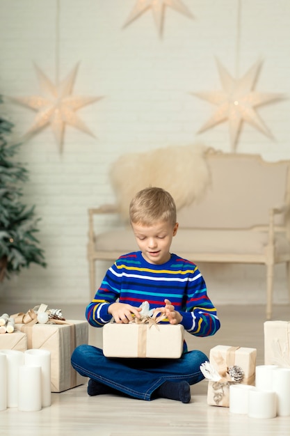 幸せな笑顔の少年は、新年の装飾を背景にクリスマスギフトボックスを保持しています。