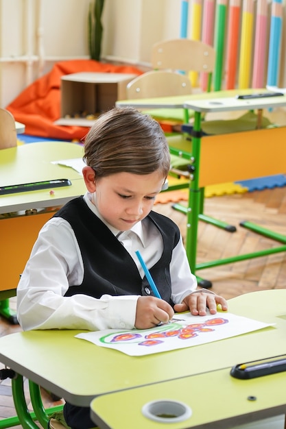 Happy smiling boy is drawing and going to school for the first time. Child with school bag and book. Kid indoors of the class room with blackboard on a background. Back to school.