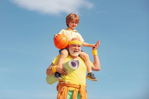 Happy smiling boy on shoulder grandpa looking at camera Senior fitness man and son training on blue background Urban modern lifestyle healthy living concept