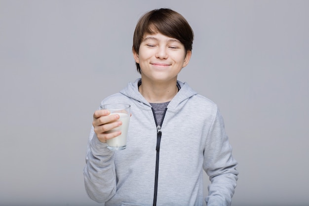 Ragazzo sorridente felice con un bicchiere di latte nelle sue mani adolescente su sfondo grigio