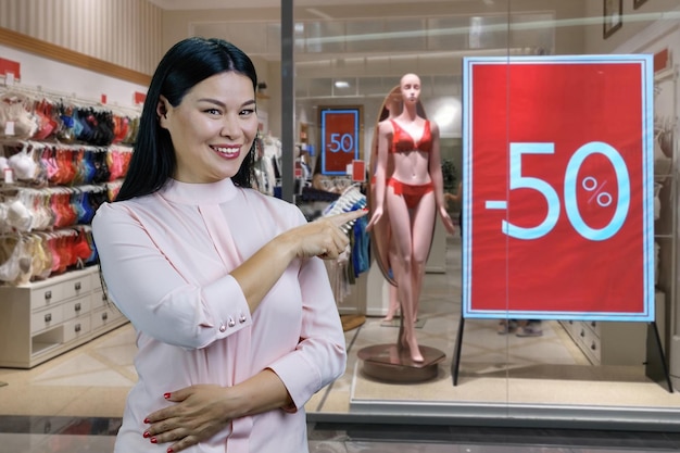 Счастливая улыбающаяся брюнетка азиатская женщина, указывающая на бутик нижнего белья