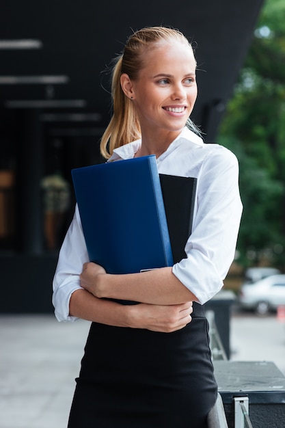 Happy smiling business woman holding folders while standing outdoors