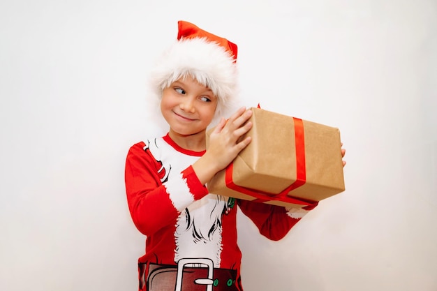 Happy smiling caucasian boy in santa tee shirt and hat holding a pox with christmas present. High quality photo