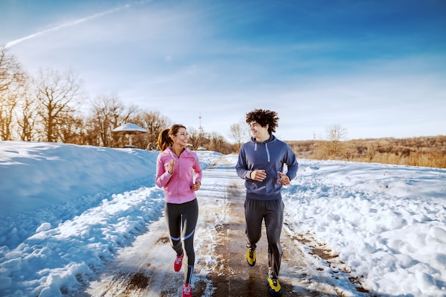 Photo happy smiling caucasian couple in sportswear running in nature while looking at each other. winter time.