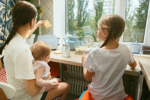 自宅で朝食時にキッチンで幸せな笑顔の白人家族。ライフスタイル、幸福、家族の概念。一緒に座っているママと2人の娘