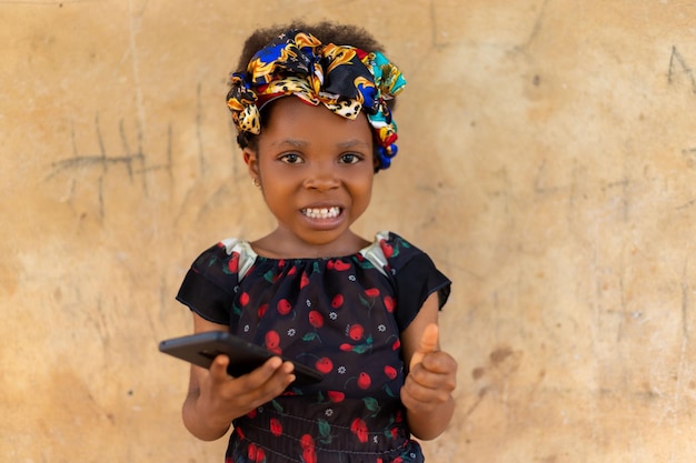 Happy smiling child girl watching in her mobile phone outdoors in summer