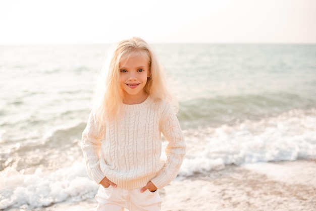 Happy smiling child girl wear white knitted sweater and pants posing over nature sea backgorund