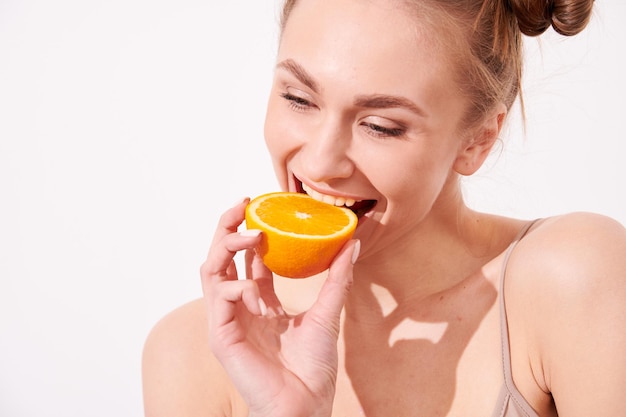 Фото Счастливая улыбающаяся женщина с чистой кожей, держащая апельсин возле лица