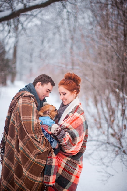 Happy smiling couple covered plaid enjoy walk with bulldog in snowy wood