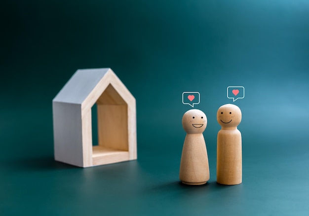 Happy smiling of couple lover wooden figure with heart symbols floating overhead standing front of miniature minimal white wood house Building family Property real estate investment concept