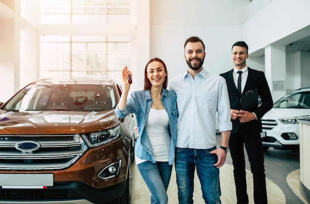 A happy smiling couple with keys in their hands from a new car looks at the camera in the dealership