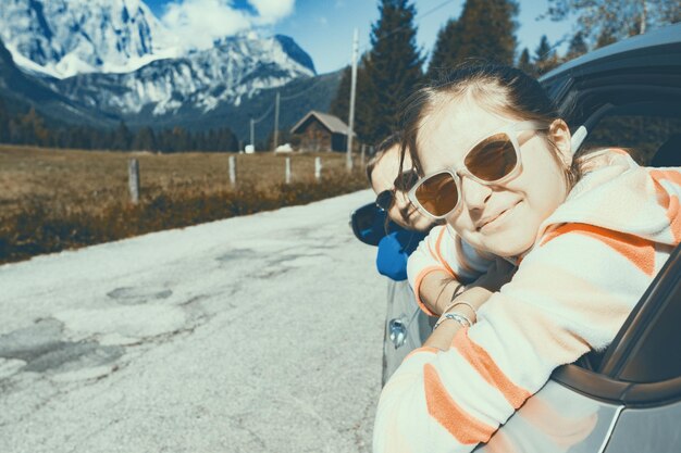 車の窓と背景の山々を眺めて幸せな笑顔のお父さんと娘。イタリア、ドロミテ