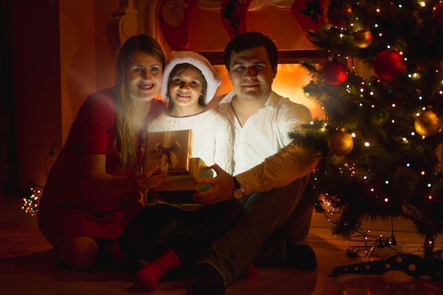 Foto famiglia sorridente felice che si siede al camino e che apre la scatola regalo di natale