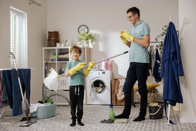 Happy smiling father and son help each other mop the floor with a mop brush and bucket