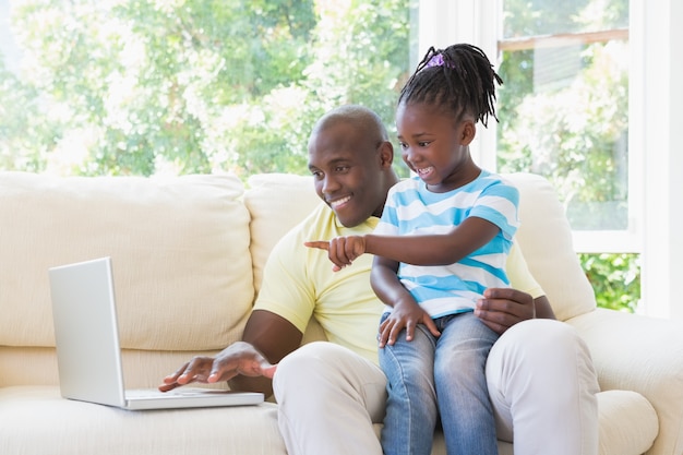 Happy smiling father using laptop with her daughter on couch 