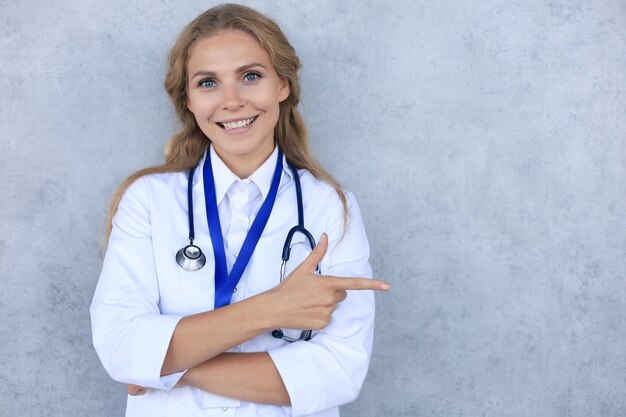 Happy smiling female doctor in white uniform coat and stethoscope, isolated over grey background.