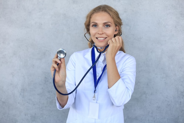 Happy smiling female doctor in white uniform coat and stethoscope, isolated over grey background.