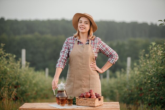 Happy smiling female farmer worker with tasty juice and fresh ripe apples in orchard garden during autumn harvest Harvesting time