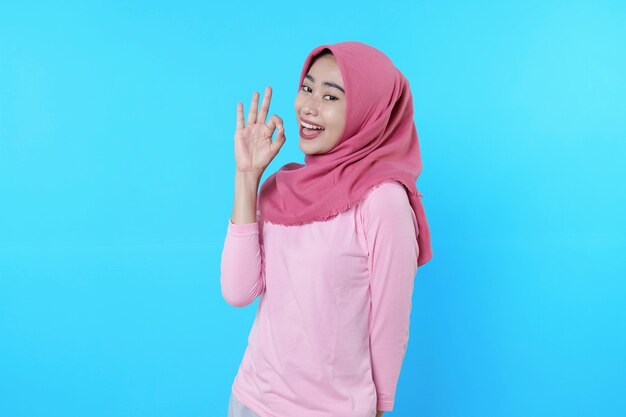 Happy smiling female with attractive appearance and wearing hijab, pink t shirt showing saying okay smile good mood