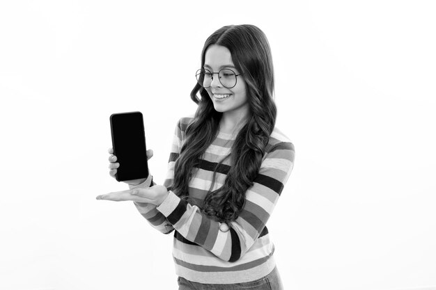 Happy smiling girl 12 13 14 years old with smart phone Hipster teen girl types message on cellphone enjoys mobile app Kid showing blank screen mobile phone mock up copy space