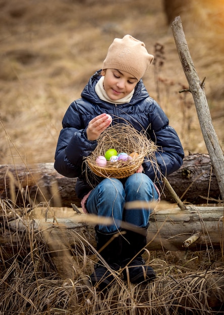 Happy smiling girl sitting on tree log at forest with Easter basket