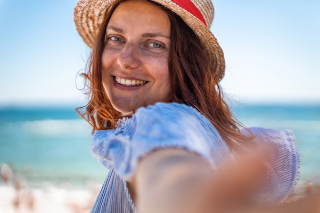 Happy smiling girl in straw hat looking at camera on the beach