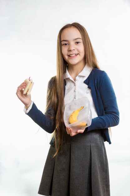 Happy smiling girl taking sandwich out of lunchbox against white background