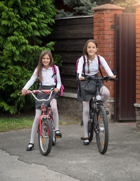 Happy smiling girls in uniform riding to school on bicycles