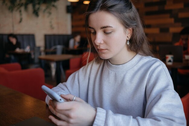 Happy smiling gorgeous woman reading pleasant text message on mobile phone sitting in coffee shop