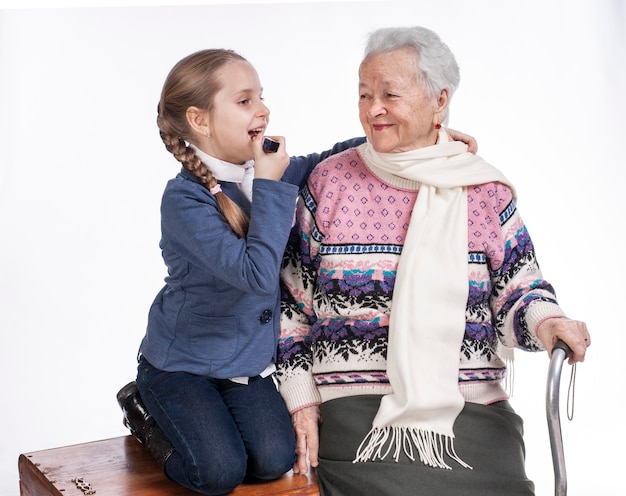 Счастливая улыбающаяся бабушка с внучкой, позирующая в студии на белом фоне. Девушка, применяющая помаду