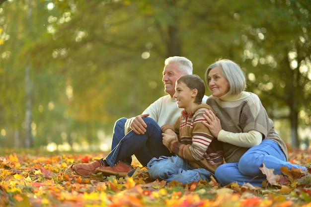 Happy smiling grandparents with their grandson in autumn forest