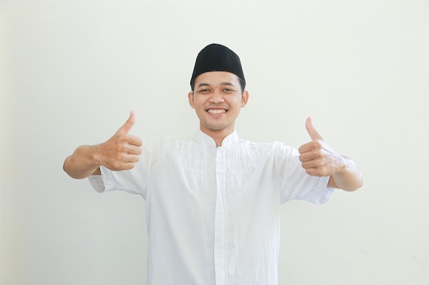 Счастливый улыбающийся красивый молодой азиатский мусульманин, показывающий большой палец вверх жестом
