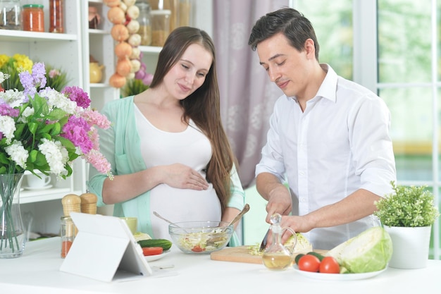 Happy smiling husband and pregnant wife cooking together in the kitchen