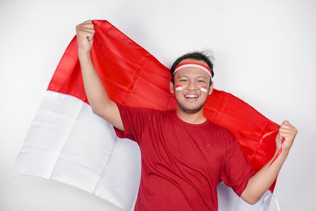 색 바탕 위에 고립된 인도네시아 독립일을 축하하기 위해 인도네시아의 발을 들고 웃는 행복한 인도네시아 남성