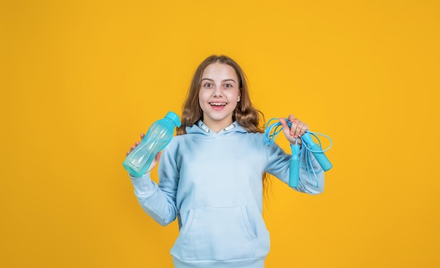 Happy smiling kid girl hold sport or fitness equipment of jumping rope and water bottle, training.