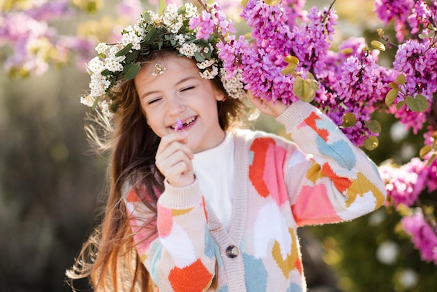행복한 미소 짓는 소녀는 화려한 스웨터와 꽃으로 장식된 화환 헤어스타일을 입습니다.