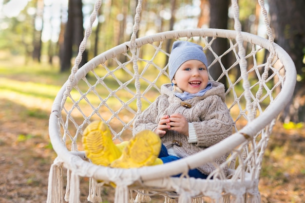 Happy smiling kid swinging in a hanging chair in a forest