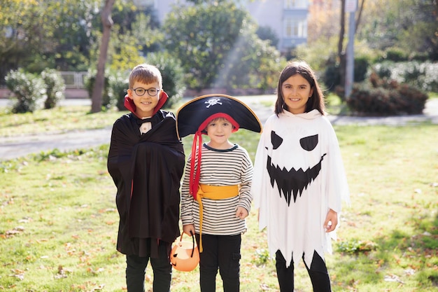 Photo happy smiling kids wearing carnival costumes of vampire pirate and ghost celebrating halloween going for treat or trick posing oudoor