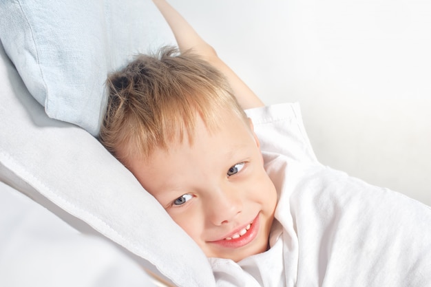 Happy smiling little boy after waking up stretching in bed. Good morning . Portrait of a white child with gray eyes and blond hair enjoying life at home.