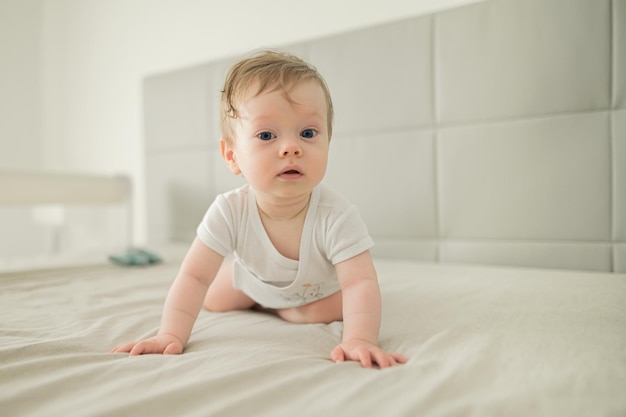 ベッドで這って家で遊んでいる幸せな笑顔の小さなかわいい幼児の男の子