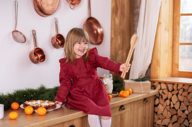 Happy smiling little girl in dress cooking Christmas cookies on kitchen at home