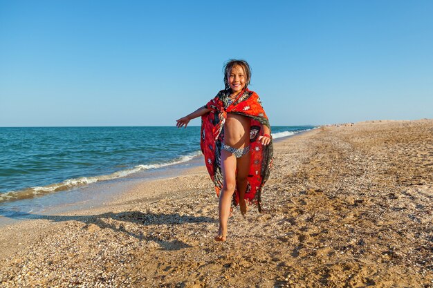 Happy smiling little girl playing with an inflatable ball on the beach by the sea shore in summer