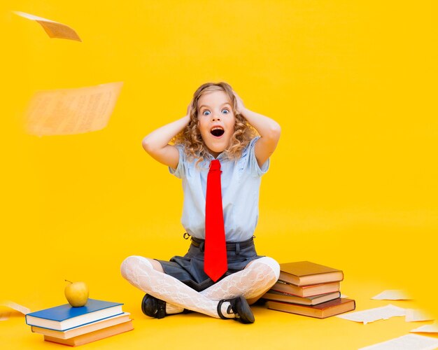 Happy smiling little girl in a school uniform sits with books,
